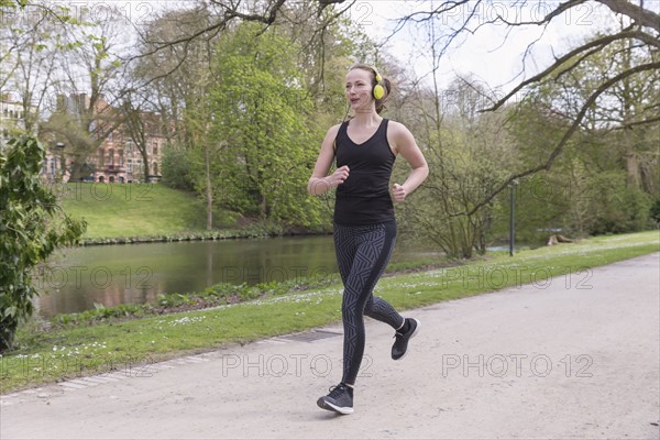 Mid-adult woman with headphones on jogging by canal in park