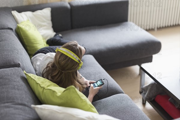 Mid-adult woman lying on sofa and listening to music from smart phone