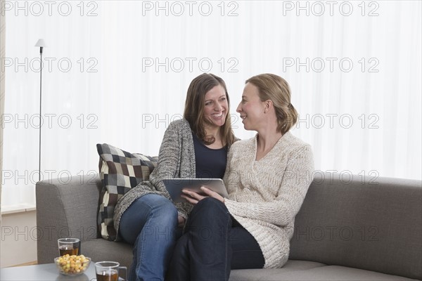 Smiling women sitting on sofa in living room and holding tablet
