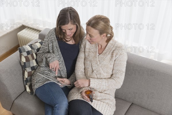 Women sitting on sofa in living room and looking at tablet