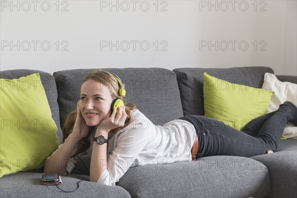 Mid-adult woman lying on sofa and listening to music from smart phone