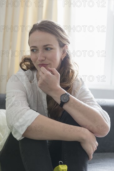 Mid-adult woman sitting on sofa with legs curled up