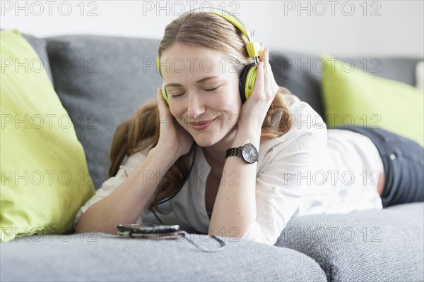 Mid-adult woman lying on sofa and listening to music from smart phone