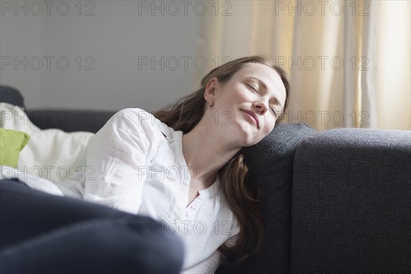 Mid-adult woman lying on sofa with closed eyes and smiling