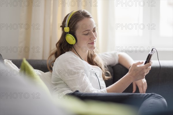 Mid-adult woman lying on sofa and listening to music from smart phone