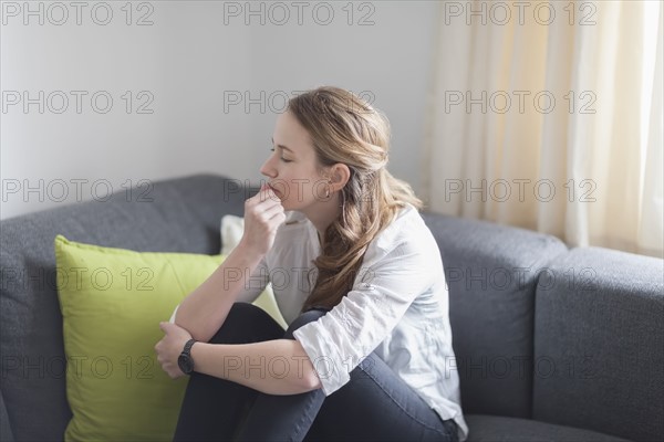 Mid-adult woman sitting on sofa with legs curled up