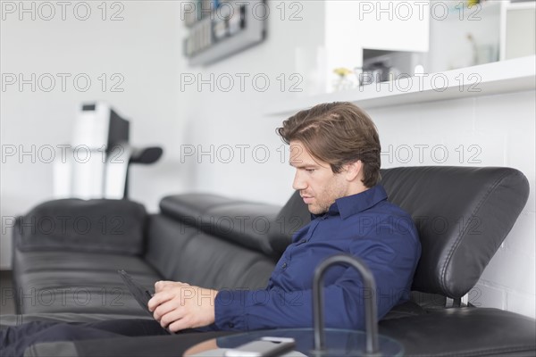 Mid-adult man sitting on sofa and using tablet