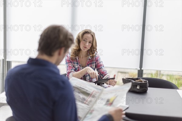 Mid-adult couple reading newspaper and using tablet at breakfast table