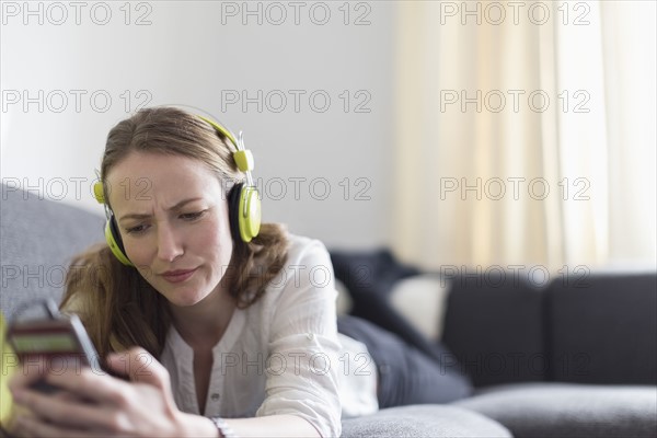 Mid-adult woman lying on sofa and listening to music from smart phone