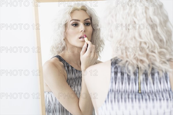 Studio shot of young woman applying lipstick.