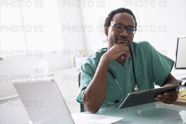 Male doctor working with digital tablet at desk.