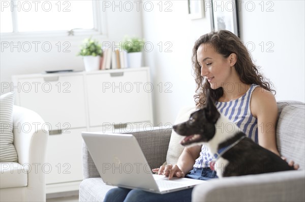 Young woman sitting on sofa with laptop and dog.