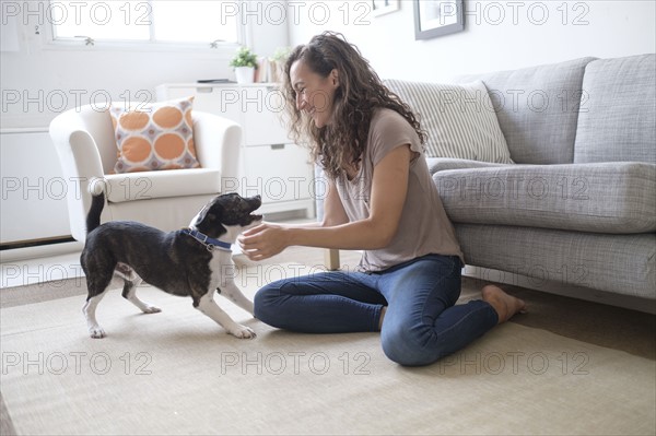 Young woman playing with dog in living room.