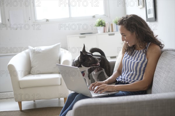 Young woman sitting on sofa with laptop and dog.