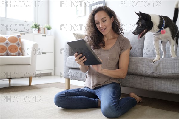 Young woman in living room using digital tablet with her dog.