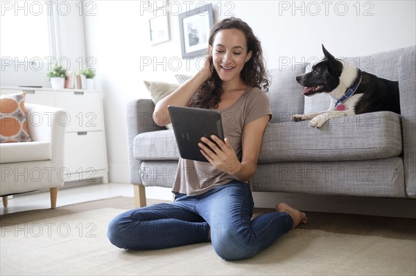 Young woman in living room using digital tablet with her dog.