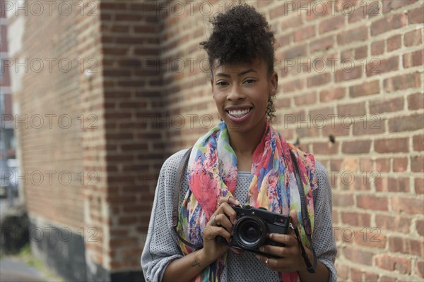 Young woman with digital camera against brick wall.