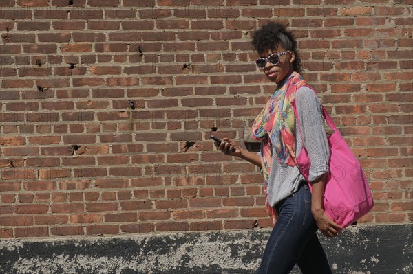 Young woman walking against brick wall.