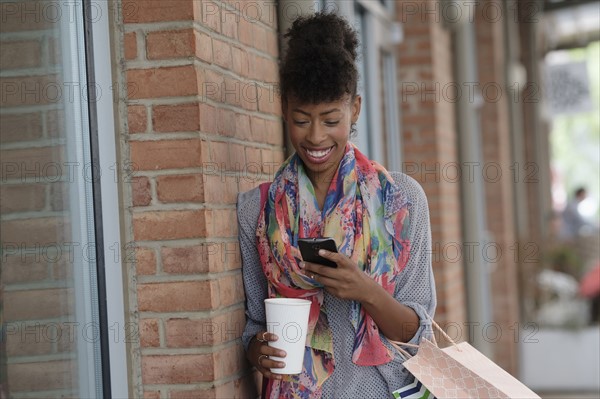 Young woman with shopping bags leaning against brick wall.