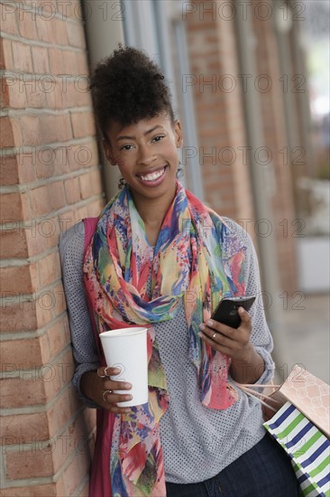 Young woman with shopping bags leaning against brick wall.