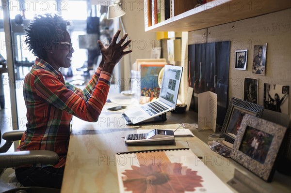 Woman gesturing in front of laptop in office.