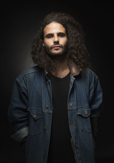 Portrait of man in denim jacket on black background.