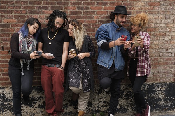 Portrait of friends using smartphones against brick wall.
