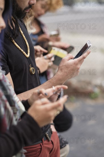 Young people standing in row using smartphones.