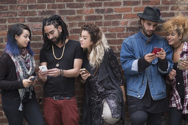 Portrait of friends using smartphones against brick wall.