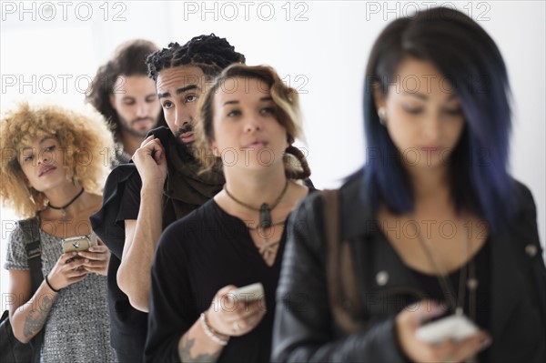 Young people standing in line using smartphones.