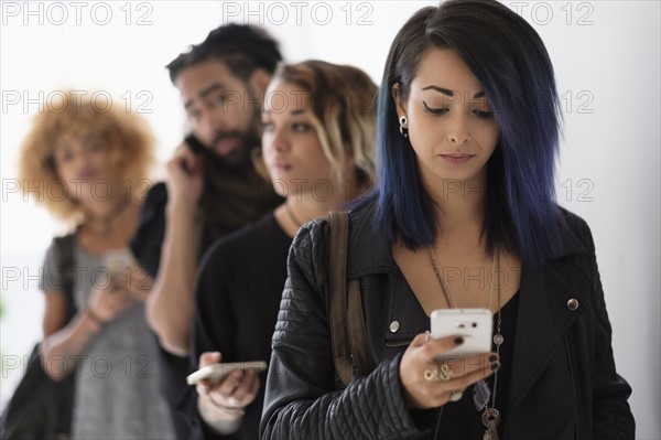 Young people standing in line using smartphones.