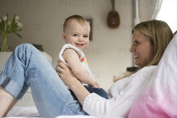 Mother and daughter (18-23 months) sitting on bed and smiling