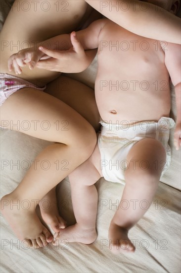 Girl (2-3) lying on bed with baby brother (6-11 months)