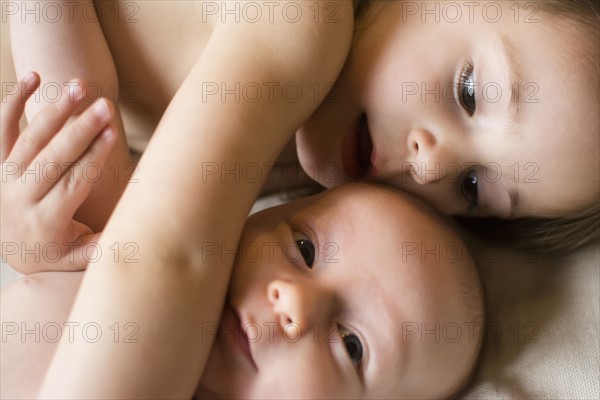 Girl (2-3) lying on bed with baby brother (6-11 months)