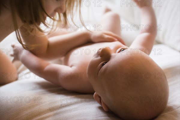 Girl (2-3) touching baby brother (6-11 months) lying on bed
