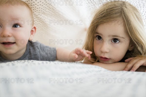 Girl (2-3) and baby brother (6-11 months) hiding under bed covers