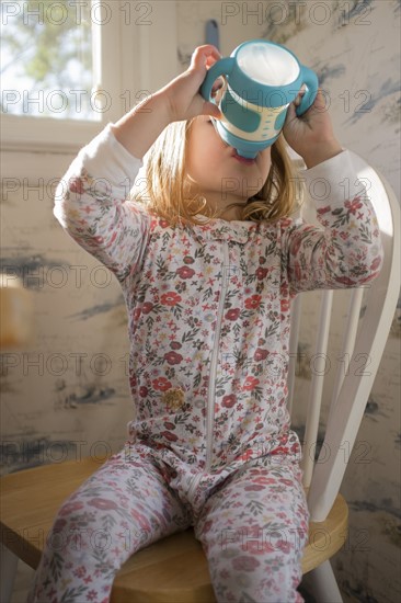 Girl (2-3) sitting on chair and drinking milk from sippy cup