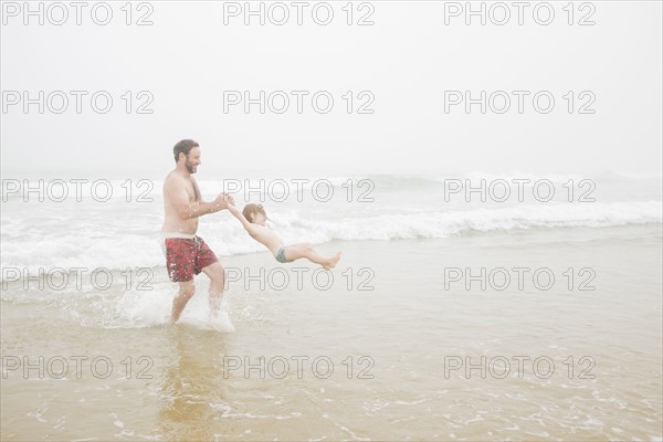 USA, New York, Monatuk, Father spinning daughter (2-3) on beach by ocean