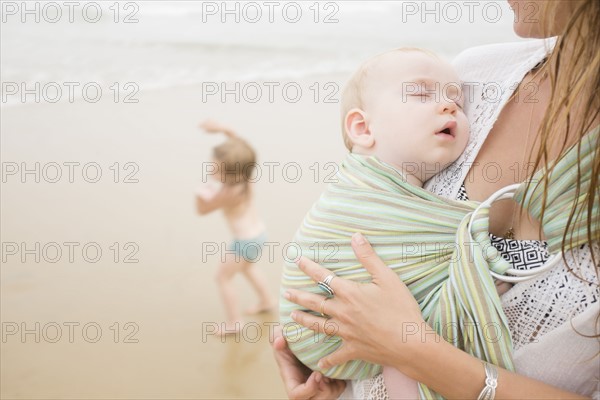 Mother holding baby son (6-11 months), daughter (2-3) dancing on beach