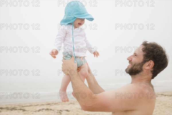 Father lifting baby son (6-11 months) on beach