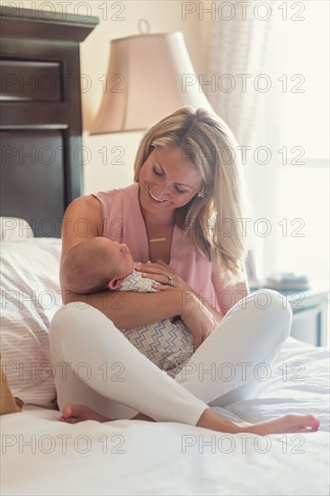 Mother sitting on bed and holding baby son (0-1 months)