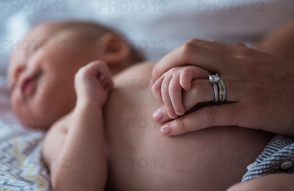 Mother holding son's (0-1 months) hand in bedroom