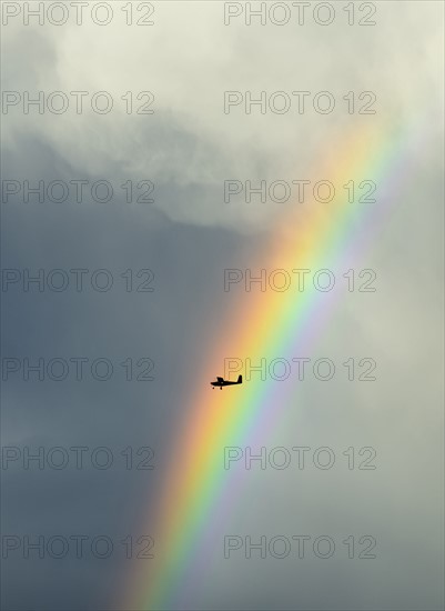 Silhouette of small plane flying through rainbow