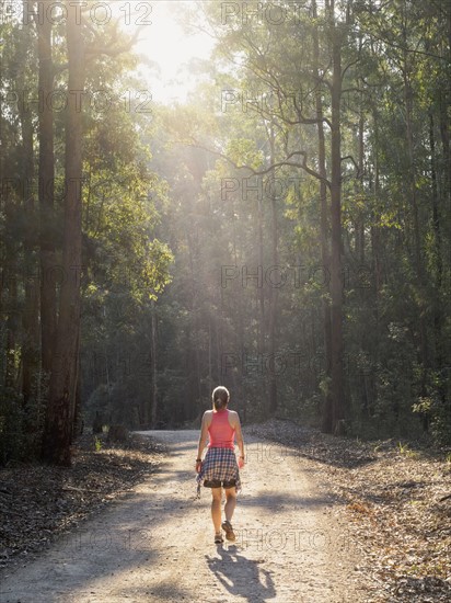 Australia, New South Wales, Port Macquarie, Rear view of mature woman walking along dirt road in forest