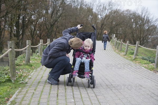 Mother talking to daughter (4-5) sitting in stroller, boy (8-9) walking in background