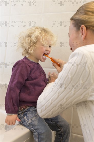 Mother brushing daughter's teeth (4-5) in bathroom