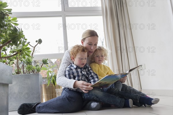 Mother reading to children (4-5, 8-9) in living room