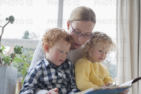 Mother reading to children (4-5, 8-9) in living room