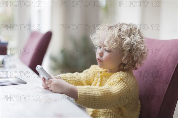 Blond girl (4-5) sitting at table and looking at mobile phone