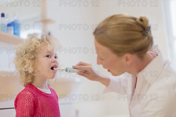 Mother helping daughter (4-5) brush teeth
